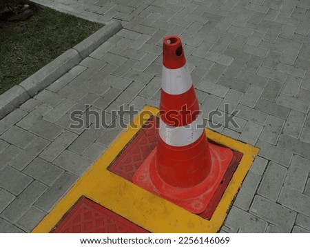 Orange cone with white signage tape on top of a red metal cap and a yellow sidewalk safety sign