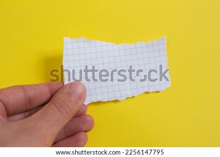 Hand holding blank checkered paper on yellow background. Top view, copy space.