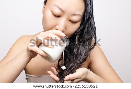 Smiling young Asian woman applying hair mask in a bathroom; haircare concept. Royalty-Free Stock Photo #2256150521