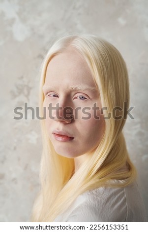 Young beautiful albino woman with no makeup looking at camera while standing over marble wall and posing during photo session