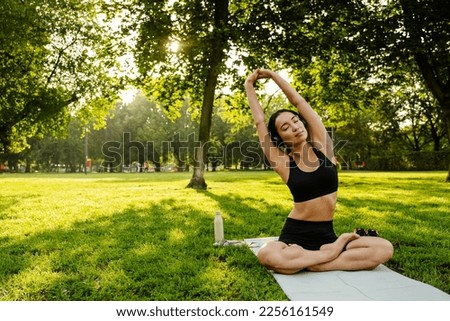 Young brunette asian woman practicing yoga during workout in park Royalty-Free Stock Photo #2256161549