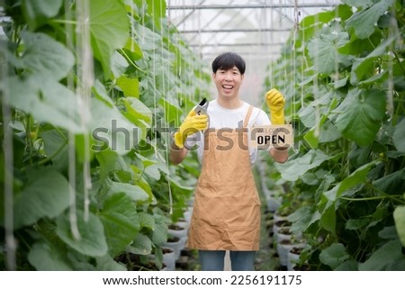 Farm owner man holding wooden sign with open letter and branch scissor looking at camera with smile of happiness, taking care, smart farm concept.