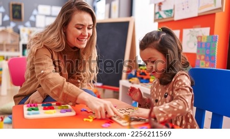 Teacher and toddler playing with maths puzzle game sitting on table at kindergarten Royalty-Free Stock Photo #2256211569