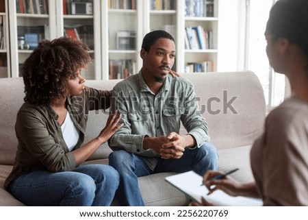 Loving attractive young black woman embracing her depressed frustrated husband looking at copy space, african american couple have therapy session with family psychologist. Marital crisis concept Royalty-Free Stock Photo #2256220769