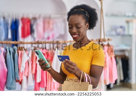 African american woman customer holding shopping bags using smartphone and credit card at clothing store
