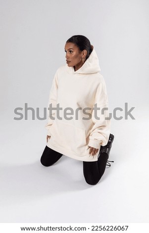 Attractive african american woman in oversized white hoodie sits on white background. Mock-up..