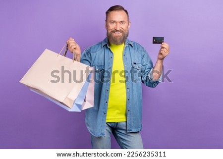 Photo of handsome aged man hold boutique bags debit plastic card isolated on violet color background