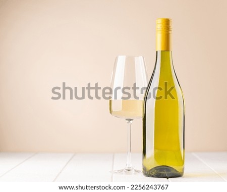 White wine bottle and glass in front of beige background. With copy space