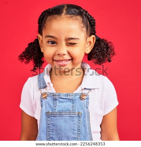 Portrait, wink and a black child on a red background in studio having fun or feeling carefree. Kids, fashion and smile with a happy female child winking inside on a color wall while looking funny Royalty-Free Stock Photo #2256248353