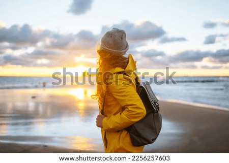 Happy tourist in a yellow jacket enjoying sea landscape at sunset. Lifestyle, travel, tourism, nature, active life. Royalty-Free Stock Photo #2256257603