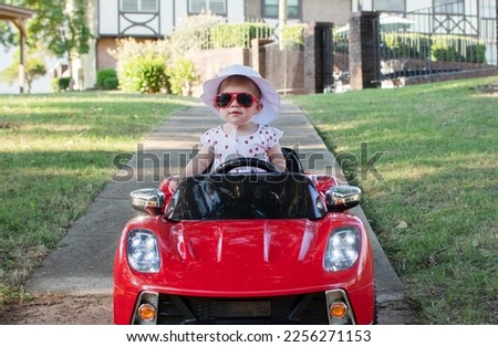 Caucasian baby in a white hat riding in an electric convertible red sports car. child driving a car on a summer day	 Royalty-Free Stock Photo #2256271153