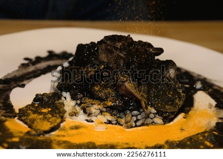 Picture of a squid recipe with a rice bed all with his black ink and sprinkled with turmeric showing modern concept of food