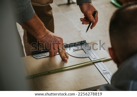 In a horizontal color image, handymen measure the wooden furniture panel with their measuring tape and protractor in an outdoor space with natural light.