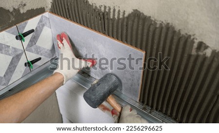 The master glues ceramic tiles on the wall in the bathroom. Adjustment of ceramic tiles with a rubber mallet. Hammer with rubber tip for ceramic tiles. Royalty-Free Stock Photo #2256296625