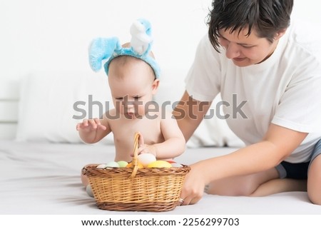 Mother and child with colorful eggs. Mom and baby with bunny ears. Parent and kid play indoors in spring. Family celebrating Easter