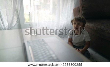 Small boy watching entertainment media cartoon sitting on floor at home staring at laptop screen