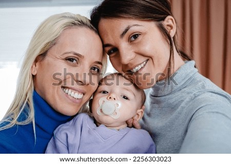 Gay lesbian couple and newborn baby taking selfie picture indoors at home - Lgbt family concept - Focus on left mother face