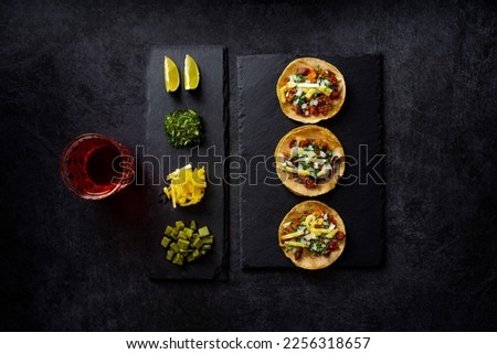 Delicious lunch with tacos and sauces on black table, top view of appetizing Mexican tacos served on black plate near bowl with tomato sauce and avocado placed on wooden table