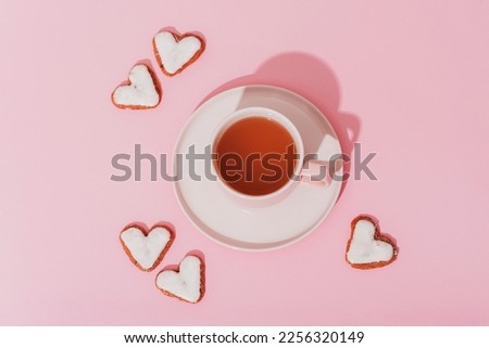 A cup of tea and heart-shaped cookies on pink background in sunlight. Valentines day concept. Top view, flat lay.