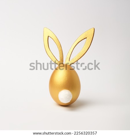 Golden Easter egg with bunny ears and tail on white background. Minimal style, side view. Happy Easter concept. Royalty-Free Stock Photo #2256320357