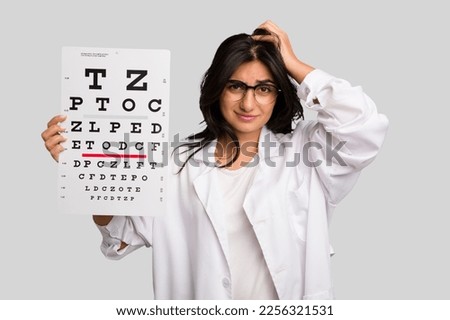Young indian oculist woman holding an eye chart paper cut out isolated being shocked, she has remembered important meeting.