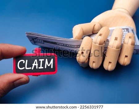 Wooden board with the word CLAIM and wooden hand holding banknotes. Business concept.
