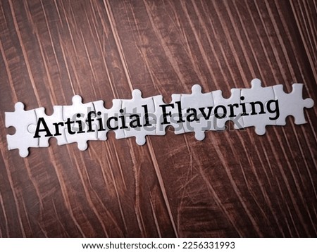 White puzzle with the word Artificial Flavoring on wooden background.