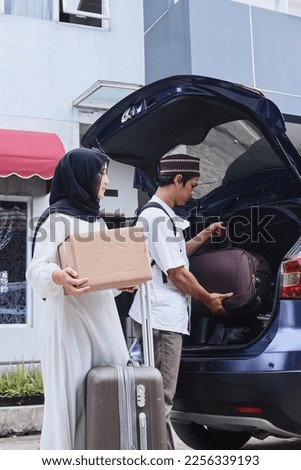 Muslim couple are moving the suitcase and cardboard box into the trunk of the car, ready to go on holiday. Mudik lebaran at Eid moment.  Royalty-Free Stock Photo #2256339193