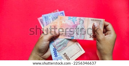 Woman holding new rupiah indonesian banknote, latest edition. Isolated on a red background
