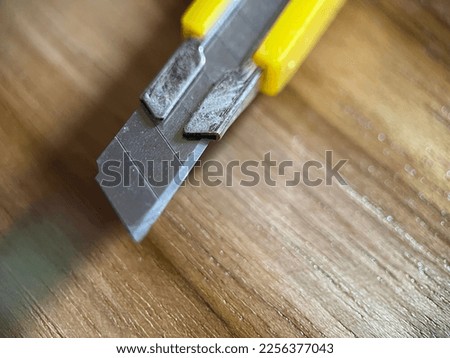 Selective focus view of yellow stationery knife with a blade on wooden background. Macro photography.