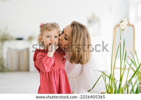 Mom kisses her three-year-old daughter on the cheek at home