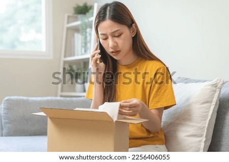 Angry bad, complaint asian young woman opening carton box, received online shopping parcel wrong product order from retail store, using mobile phone talking with support shop want to return package. Royalty-Free Stock Photo #2256406055