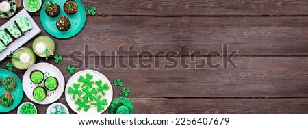 St Patricks Day theme desserts. Corner border against a dark wood banner background. Shamrock cookies, green cupcakes, brownies, donuts and sweets. Top view. Copy space.