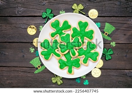 St Patricks Day shamrock cookies. Overhead view plate with frame of decor on a dark wood background.