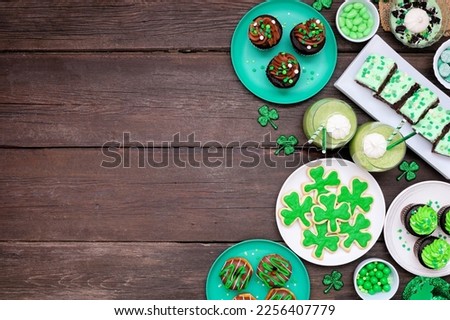 St Patricks Day theme desserts. Side border against a dark wood background. Shamrock cookies, green cupcakes, brownies, donuts and sweets. Above view. Copy space.