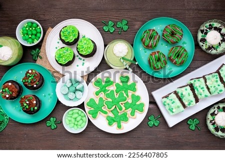 St Patricks Day theme desserts. Table scene over a dark wood background. Shamrock cookies, green cupcakes, brownies, donuts and sweets. Overhead view.