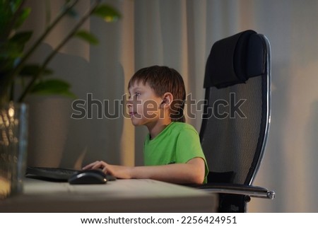 Cute caucasian boy playing video game or study at desktop computer at home. Image with selective focus