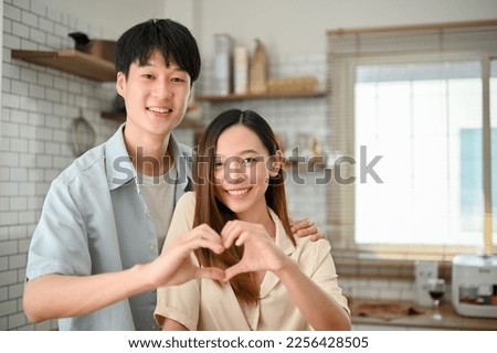 Lovely and in love young Asian couple making a heart hand sign together in the kitchen. happy relationship, girlfriend and boyfriend, togetherness 