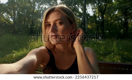 Beautiful young blonde woman makes selfie on camera on hands, POV view. cute girl sits on bench in park and looks into camera or mirror. In nature, slender girl flirts with camera.