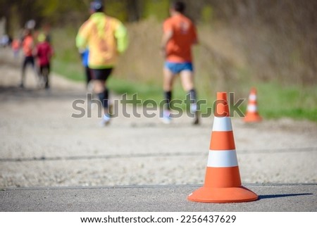 Close-up photo of a traffic cone and athletes in the background competing in a marathon, promoting a healthy lifestyle