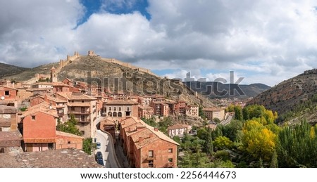 Colorful panoramic view of the medieval small village of Albarracin and its defensive wall in Autumn blue sky and white clouds background