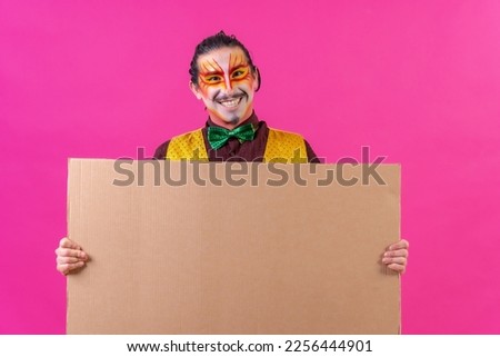 Clown with white facial makeup showing a sign on a pink background, announcing something