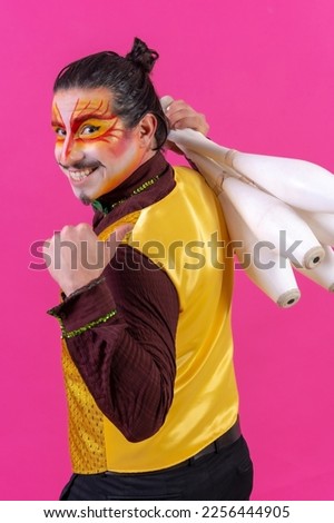 Juggler in a vest and with painted face juggling with maces on a pink background, doing ok