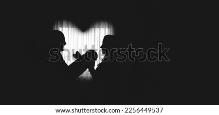 Silhouettes of happy parents, father and mother holding newborn baby by the window, heart shaped