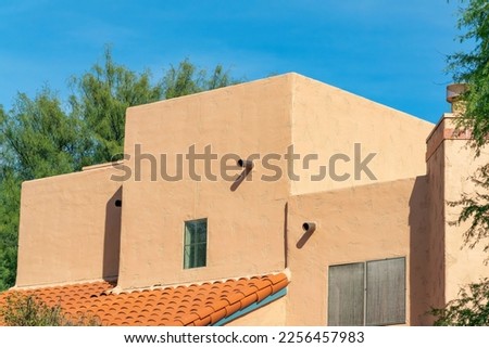 Block style building with adobe design or architecture with flat roof and red tiles and back or front yard trees in sun. Late afternoon with neighborhood in desert with mexican design on structure. Royalty-Free Stock Photo #2256457983