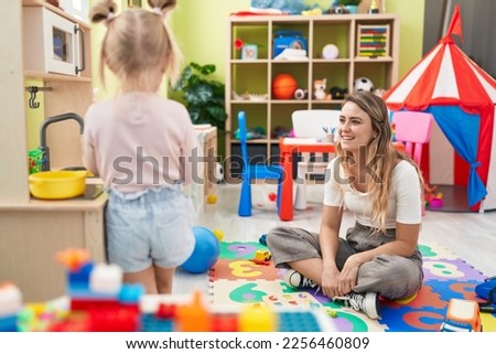 Teacher and toddler playing with play kitchen standing at kindergarten