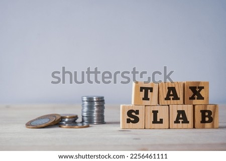 Tax slab written on wooden blocks with coins on desk.  Royalty-Free Stock Photo #2256461111