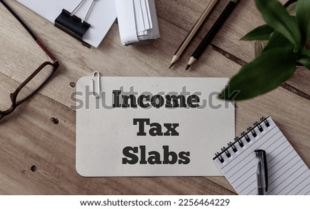 Income Tax Slabs inscription on white card. Workplace background, top view.  Royalty-Free Stock Photo #2256464229