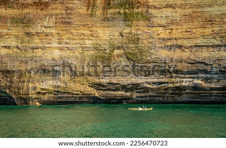 Giant granite rock wall in comparison to tiny kayak in lake northern Michigan
