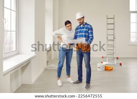 Finishing painting decorating work foreman builder supervisor in hardhat showing young woman homeowner renovation plan standing in empty house or apartment with ladder and plaster bucket in background Royalty-Free Stock Photo #2256472555